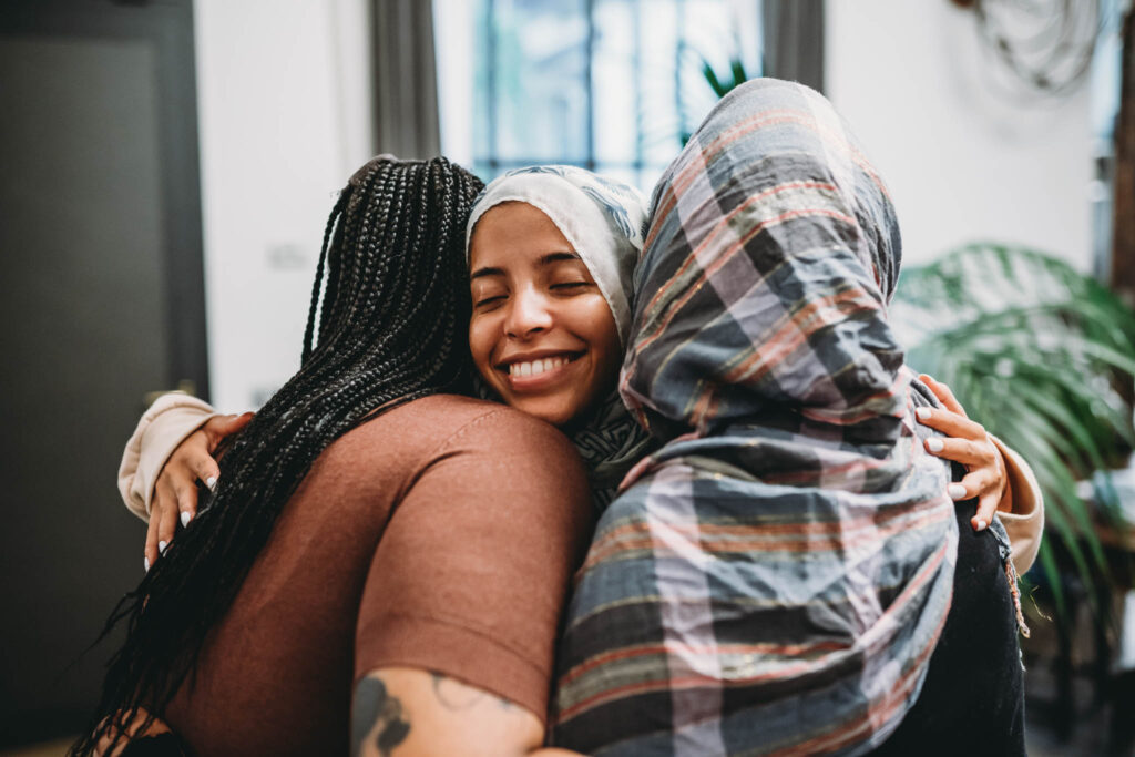 Close up shot of three friends embracing each other. They are smiling, supporting each other.